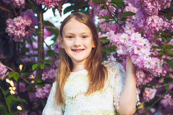 Spring portrait of a cute little girl playing at sunset with flowers of japanese cherry in blossom — Stock Photo, Image