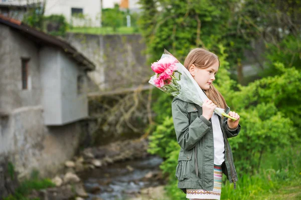 Utomhus porträtt av en söt liten flicka, klädd i khaki parka, hålla bukett rosa pioner — Stockfoto