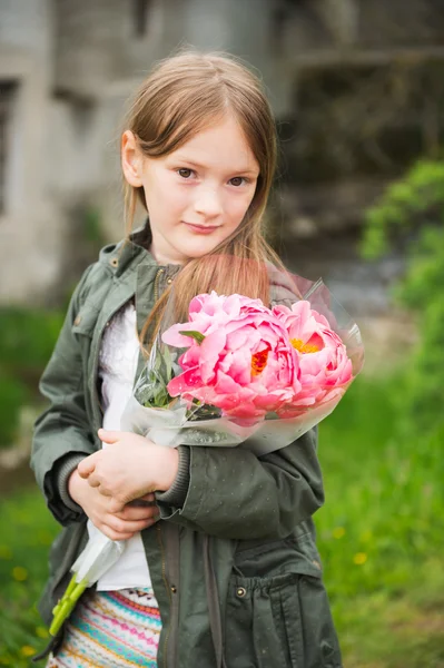 Utomhus porträtt av en söt liten flicka, klädd i khaki parka, hålla bukett rosa pioner — Stockfoto