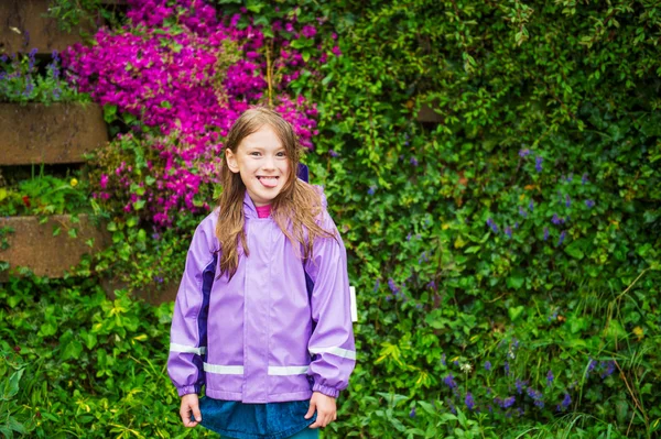 Outdoor Portret van een schattig klein meisje onder de regen, trekken haar tong, dragen paarse regenjas — Stockfoto