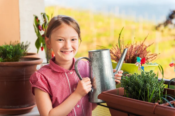 Entzückendes kleines Mädchen, das an einem schönen sonnigen Tag Pflanzen auf dem Balkon gießt — Stockfoto
