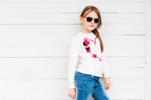 Mode portret van een schattig klein meisje tegen witte achtergrond, dragen sweatshirt en jeans — Stockfoto