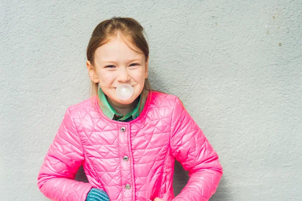 Ritratto di una graziosa bambina con gomma da masticare, indossando una giacca rosa brillante — Foto Stock