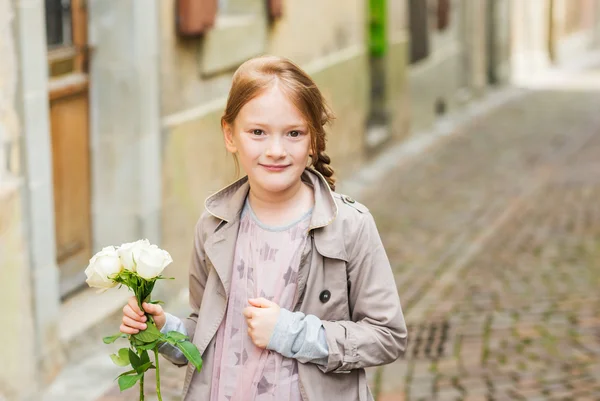 Utomhus porträtt av en söt liten flicka med vita rosor, klädd i beige päls och rosa klänning — Stockfoto