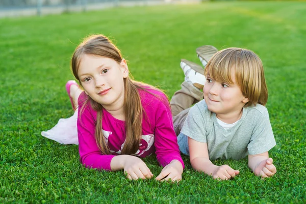 Außenporträt zweier niedlicher Kinder, die auf einem leuchtend grünen Rasen liegen — Stockfoto