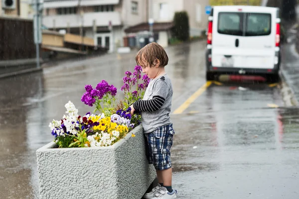 Söt liten pojke spelar under regn i en stad — Stockfoto