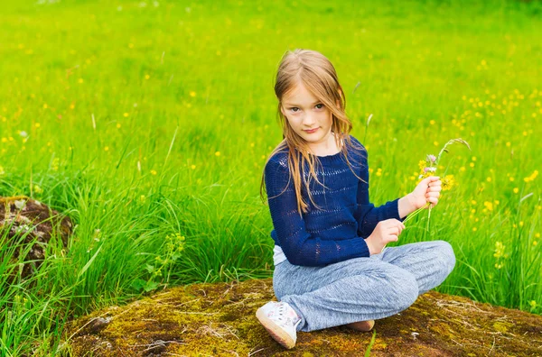 Retrato ao ar livre de uma menina bonito descansando na natureza, brincando com flores, vestindo pulôver azul e calças cinza — Fotografia de Stock