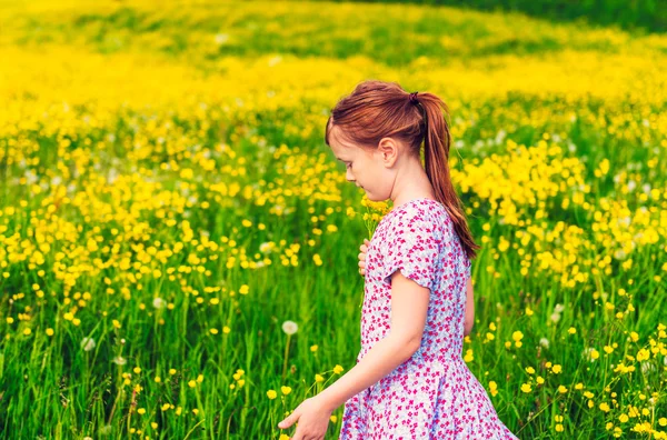 Bedårande liten flicka på 7 år gammal spelar i fältet full av gula smörblommor, iklädd sommarklänning — Stockfoto