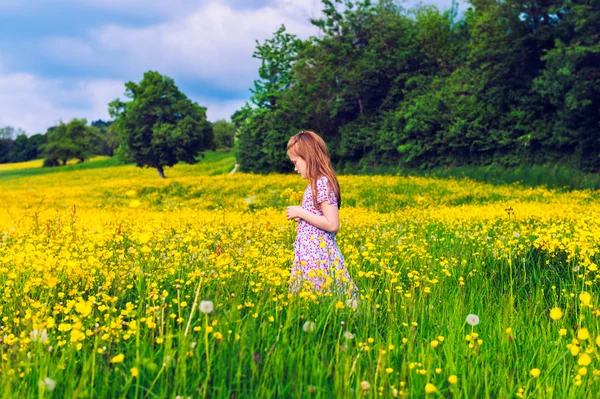 Adorable little girl of 7 years old playing in field full of yellow buttercups, wearing summer dress — Stock Photo, Image