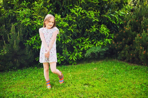 Zewnątrz portret ładny małej dziewczynki gry w ogrodzie po deszczu, noszenie letnią sukienkę i kolorowe kalosze — Zdjęcie stockowe