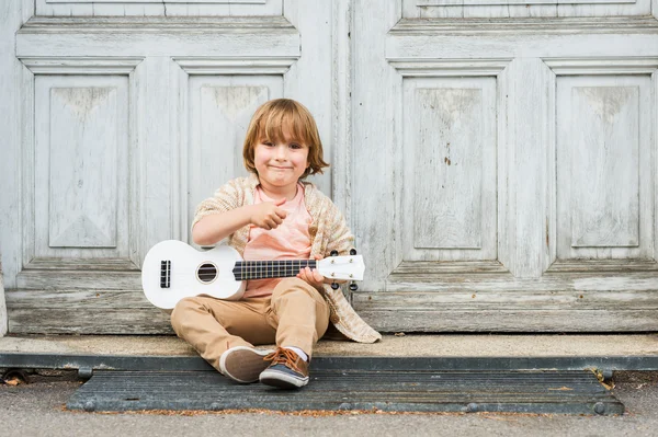 küçük mutlu çocuk onun gitar ya da açık havada ahşap kapının yanında oturmuş ukulele, çalış