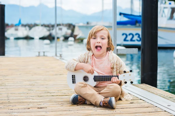 Szczęśliwy chłopiec gra jego gitara lub ukulele, siedzi nad jeziorem — Zdjęcie stockowe