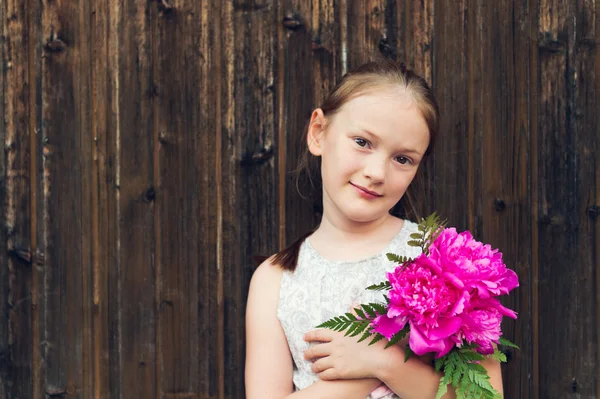 Närbild porträtt av en söt liten flicka med vackra rosa pioner — Stockfoto