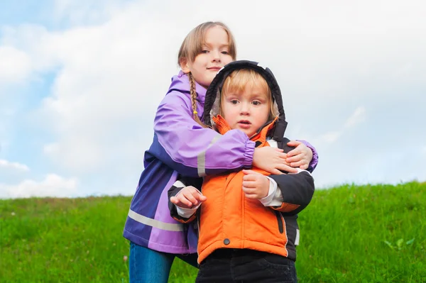 Kültéri álló, két aranyos gyerek meleg kabátot visel — Stock Fotó
