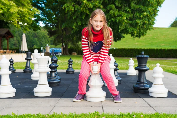 Adorável menina brincando com xadrez enorme em um parque em um dia agradável — Fotografia de Stock