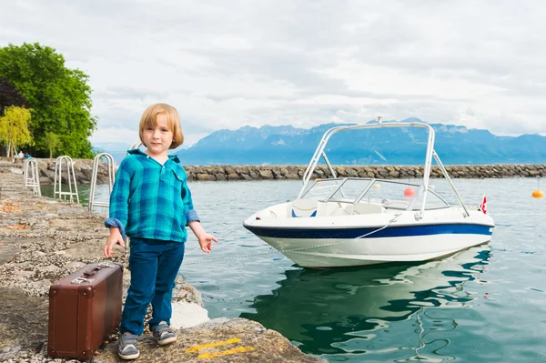 Entzückender kleiner blonder Junge mit kleinem alten Koffer, der auf einem Steg steht und bereit ist, auf dem Boot zu reisen — Stockfoto