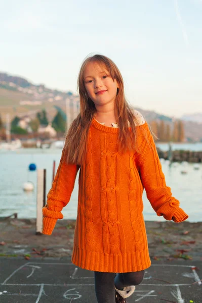 Portrait of a cute little girl playing outdoors, wearing bright big orange mother's pullover — Stock Photo, Image