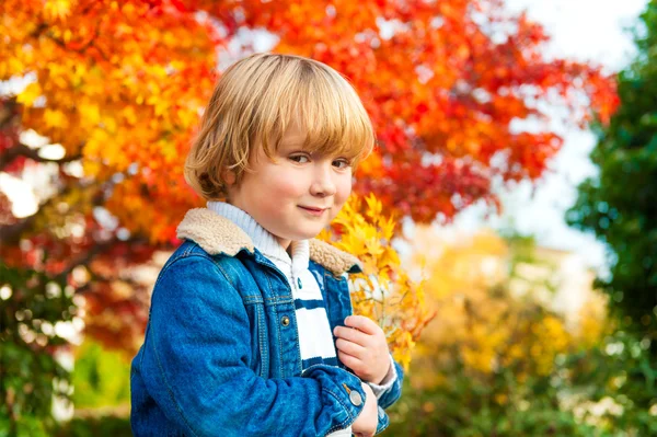 Höstens porträtt av en söt liten knatte pojke, klädd i denim kappa och varm tröja, spelar med ljusa lönn löv — Stockfoto