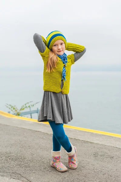 Menina bonito se divertindo ao ar livre em um dia frio, dançando ao lado de belo lago, vestindo pulôver de lã verde, chapéu e botas quentes — Fotografia de Stock