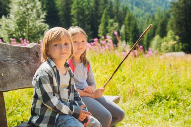 Cute little boy and his sister with backpack hiking in mountains, resting on a bench