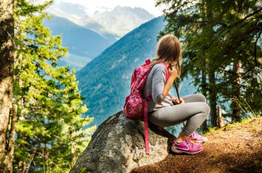 Cute little girl hiking in swiss Alps, resting on a rock and admire amazing view