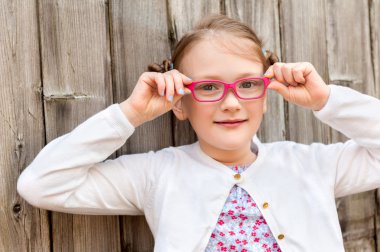 Ahşap arka plan üzerinde duran pembe gözlük takan bir sevimli küçük kız 7 yaşında portresi kapatın