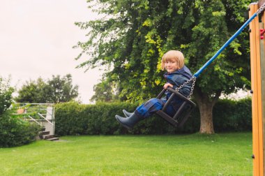 Yağmurlu bir gün bir salıncak üzerinde eğleniyor, mavi waterpoof tüm-içinde-bir takım elbise sevimli çocuk