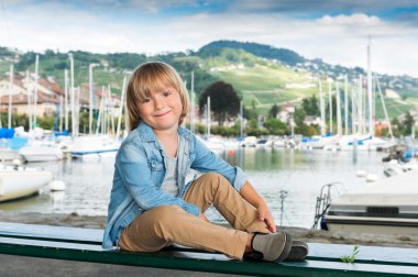 Kot gömlek ve bej pantolon giyen gölün, bir bankta oturmuş bir şirin küçük sarışın çocuk moda portre