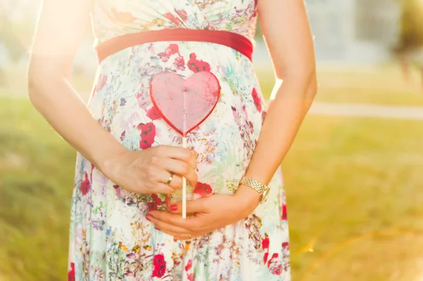 Mulher grávida segurando doces em forma de coração ao lado de sua barriga — Fotografia de Stock