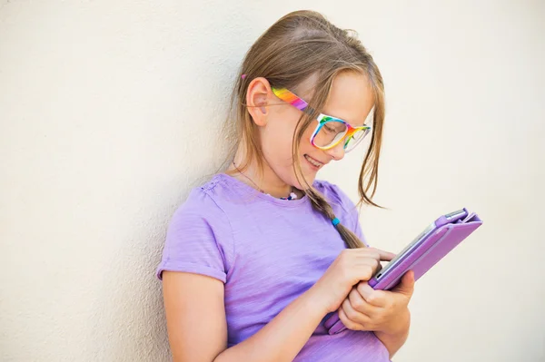 Adorável menina brincando em um tablet digital, usando óculos de arco-íris — Fotografia de Stock