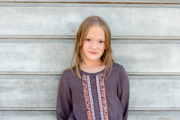 Close up portrait of a cute little girl of 8 years old against grey wooden background, wearing brown blouse — Stockfoto