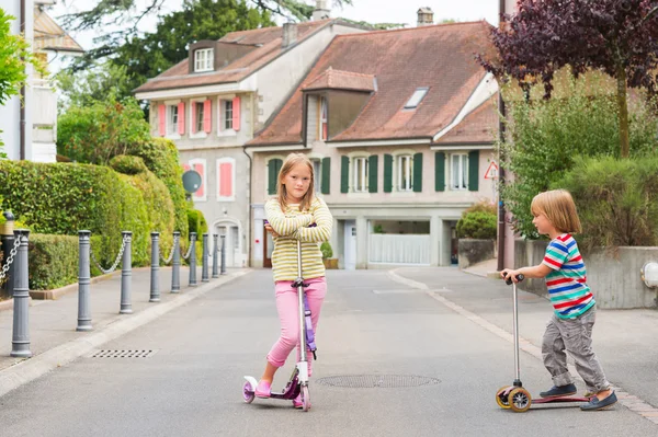 Two cute kids playing outdoors, riding scooters — Stock Photo, Image