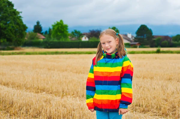 Adorabile bambina che gioca in un campo, indossa un impermeabile arcobaleno — Foto Stock