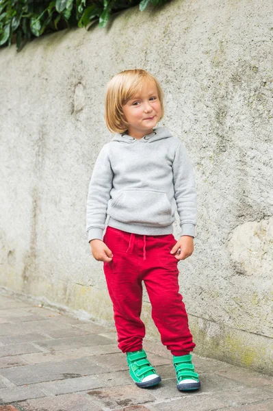 Модный портрет очаровательного мальчика в серой толстовке, красных тренировках и зеленых туфлях — стоковое фото