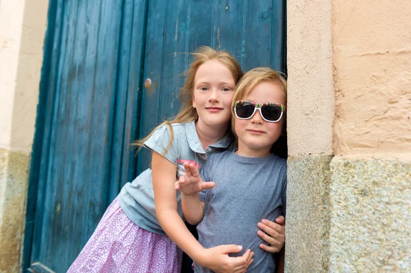 Outdoor portrait of cute kids, little girl and her brother, wearing grey tees, standing against blue wall. Tourists in Europe — ストック写真