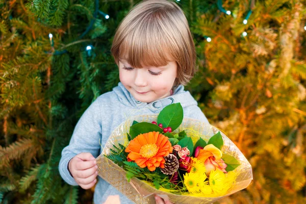 Retrato de um menino bonito segurando buquê de flores de Natal, de pé ao lado da árvore de Natal — Fotografia de Stock