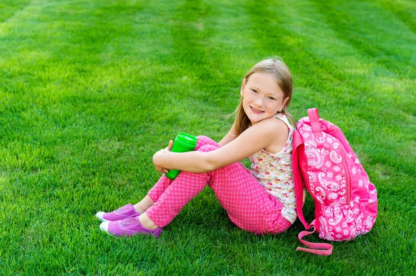 Cute młoda dziewczyna odpoczynek po szkole, siedząc na jasny zielony trawnik, powrót do koncepcji szkoły — Zdjęcie stockowe