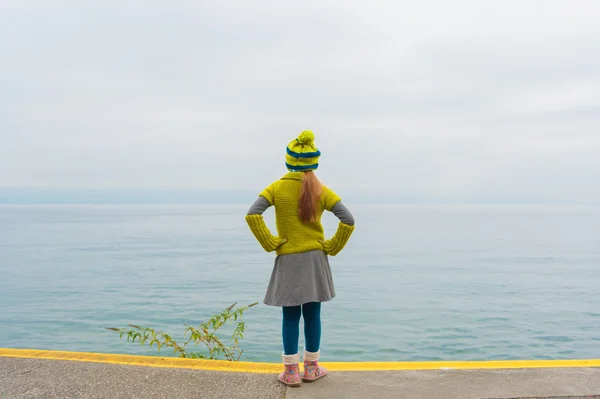 Cute little girl standing next to beautiful lake on a cold day, back view, wearing warm knit pullover and hat, boots — 스톡 사진