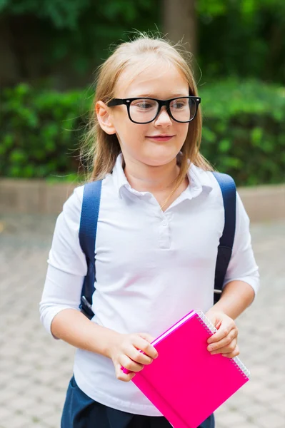 Niedliches kleines Mädchen mit Rucksack, in der Hand ein rosa Notizbuch, Outdoor-Porträt, trägt weißes Top und schwarzen Rock — Stockfoto