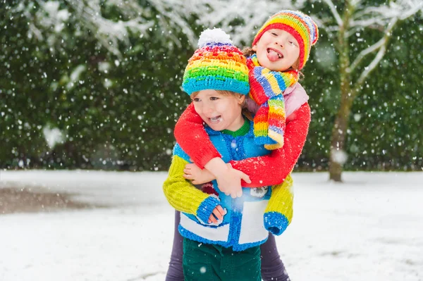Barn i färgglada kläder spelar i parken under snöfall, klädd i färgglada stickade plagg — Stockfoto