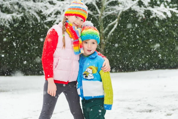 Barn i färgglada kläder spelar i parken under snöfall, klädd i färgglada stickade plagg. — Stockfoto