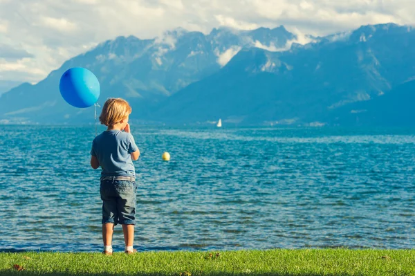 Ładny mały chłopiec gra przez jeziora, trzymając balon niebieski — Zdjęcie stockowe