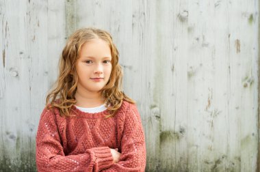 Gri ahşap arka plan üzerinde oturan pişmiş toprak kazak giyen sevimli küçük bir kız kıvırcık saçlı, 8 yaşında portresi kapatın