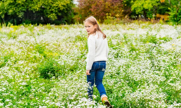 Nettes kleines Mädchen spielt auf einem Feld, trägt warmen weißen Pullover und Jeans — Stockfoto