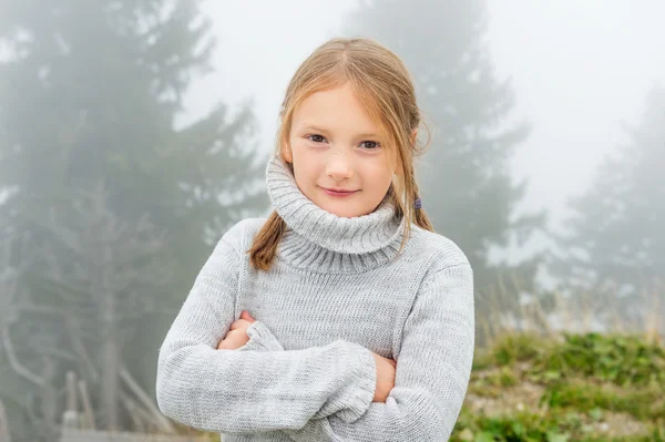 Cute little girl of 8 years old playing outdoors on a very foggy day, wearing grey warm pullover
