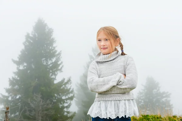Симпатичная девочка 8 лет, играющая на улице в очень туманный день, в сером теплом пуловере — стоковое фото