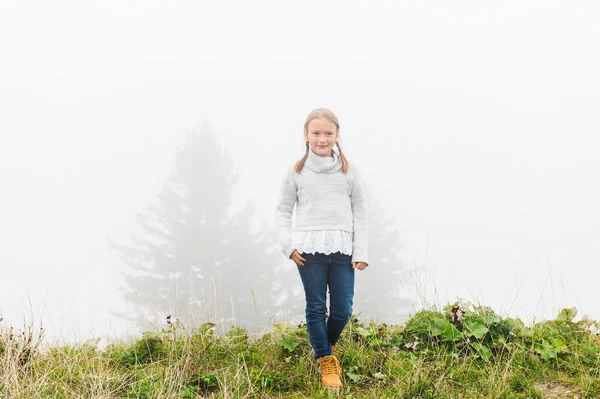 Cute little girl of 8 years old playing outdoors on a very foggy day, wearing grey warm pullover — ストック写真