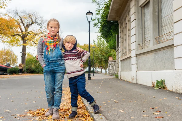 Autumn portrait of 2 adorable kids in a city, wearing warm pullovers and denim jeans — Stock Photo, Image