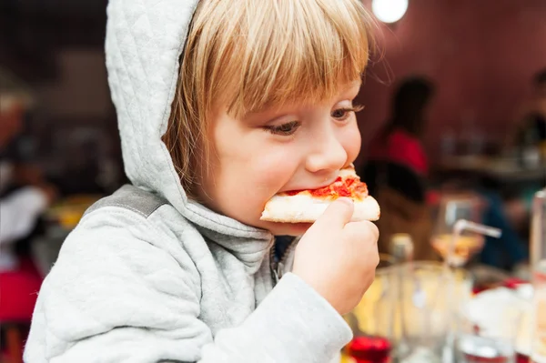 Cute little boy eating pizza in the restaurant