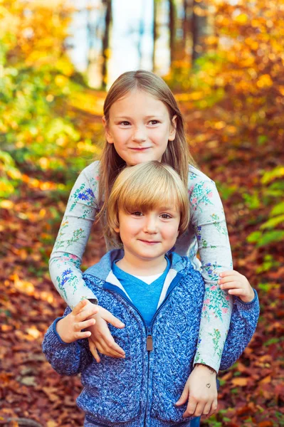 Podzimní portrét roztomilý dívka a její bratříček, hraje v lese — Stock fotografie